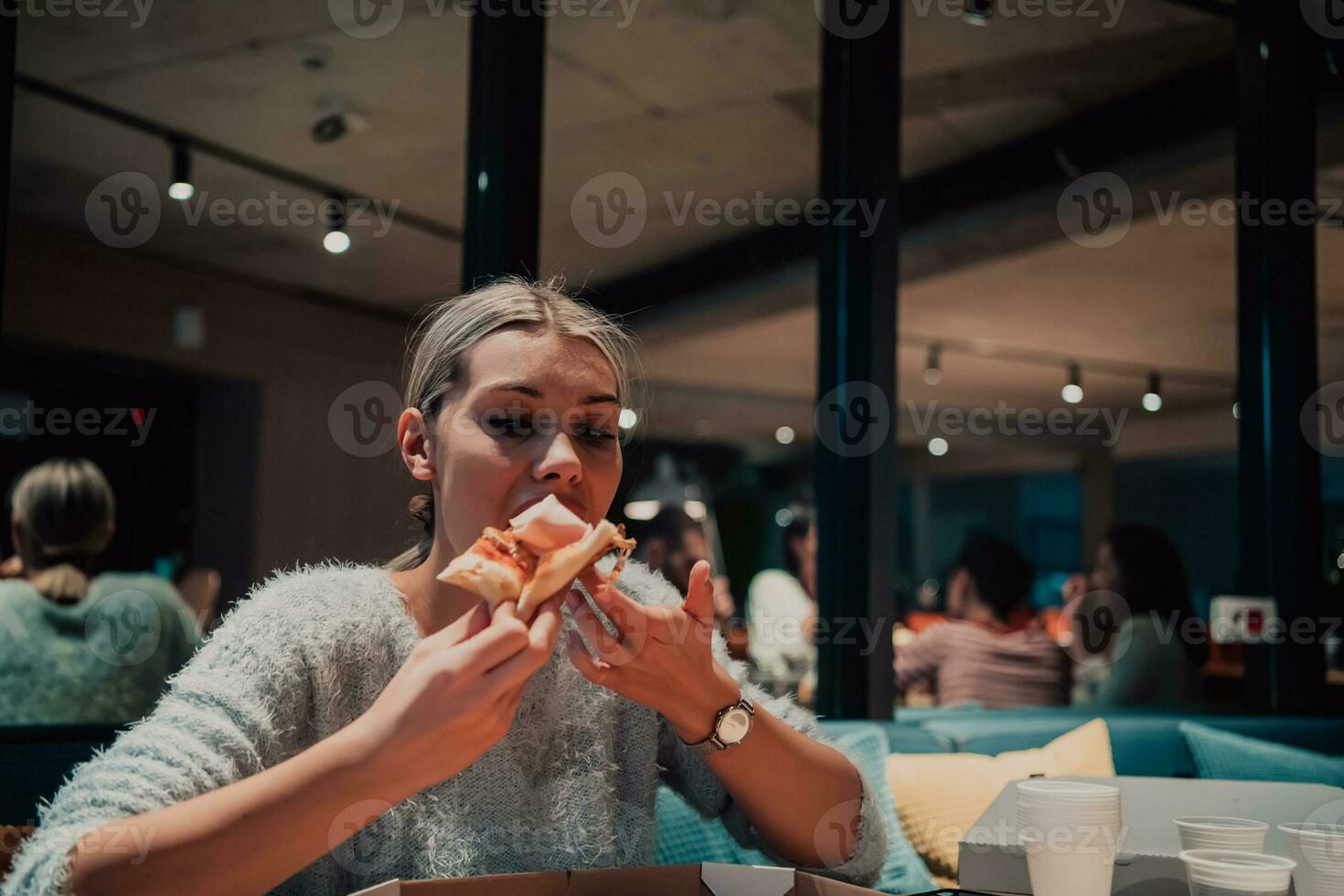 un' moderno bionda mangiare Pizza nel sua ufficio su un' rompere a partire dal opera foto