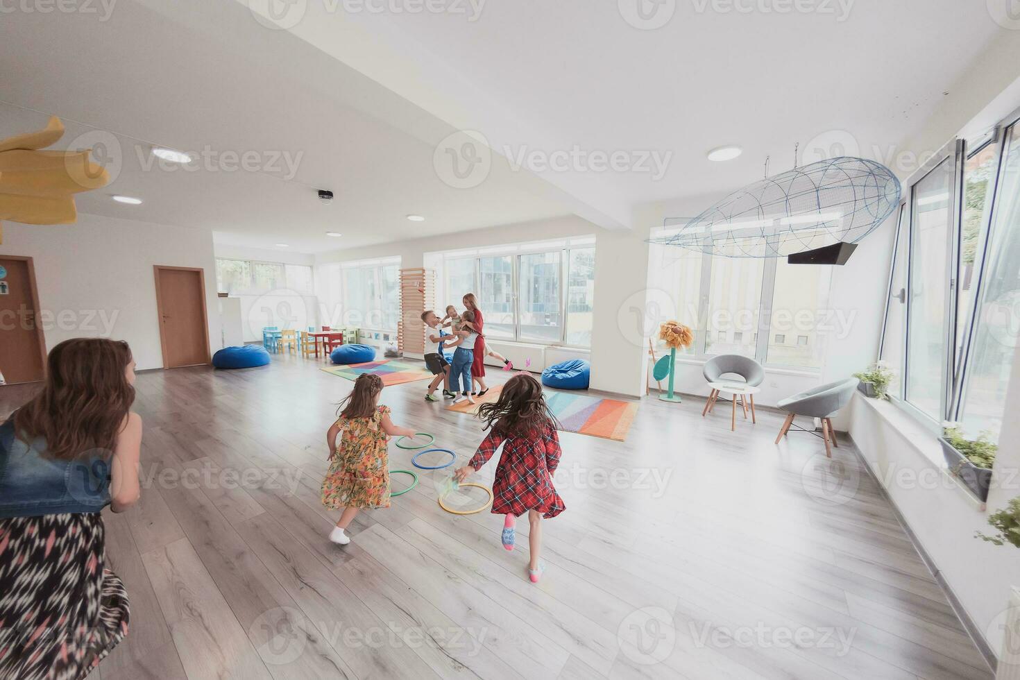 piccolo asilo scuola bambini con femmina insegnante su pavimento in casa nel aula, fare esercizio. salto al di sopra di hula cerchio cerchi traccia su il pavimento. foto