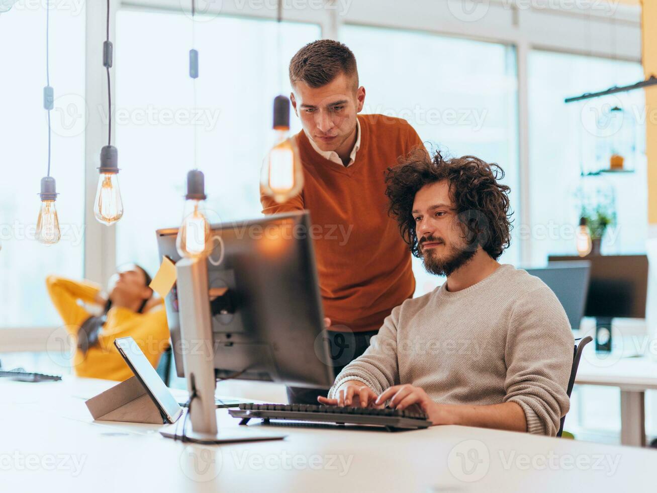 Due uomini discutere un' progetto mentre guardare a un' computer tenere sotto controllo nel un' moderno ufficio foto