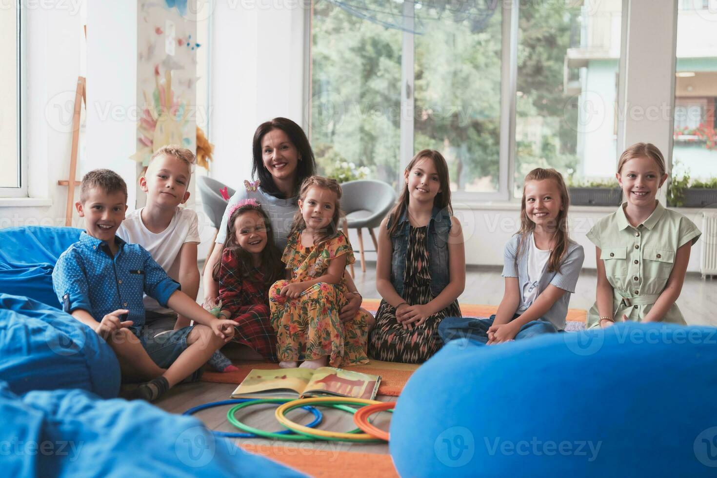 un' contento femmina insegnante seduta e giocando mano Giochi con un' gruppo di poco scolari foto