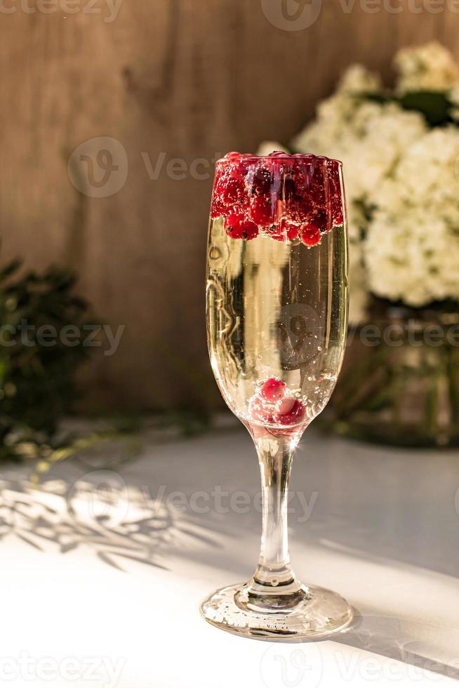 spumante nel bicchiere con bacche di ribes rosso foto