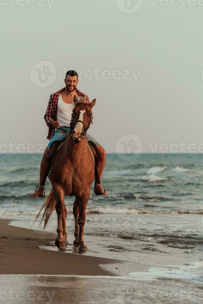 un' moderno uomo nel estate Abiti gode equitazione un' cavallo su un' bellissimo sabbioso spiaggia a tramonto. selettivo messa a fuoco foto