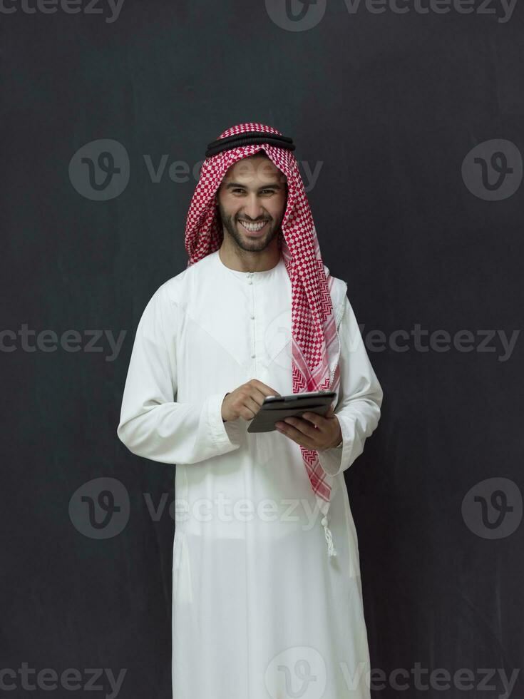 giovane arabo musulmano uomo d'affari utilizzando tavoletta computer indossare hijab Abiti nel davanti di nero lavagna foto