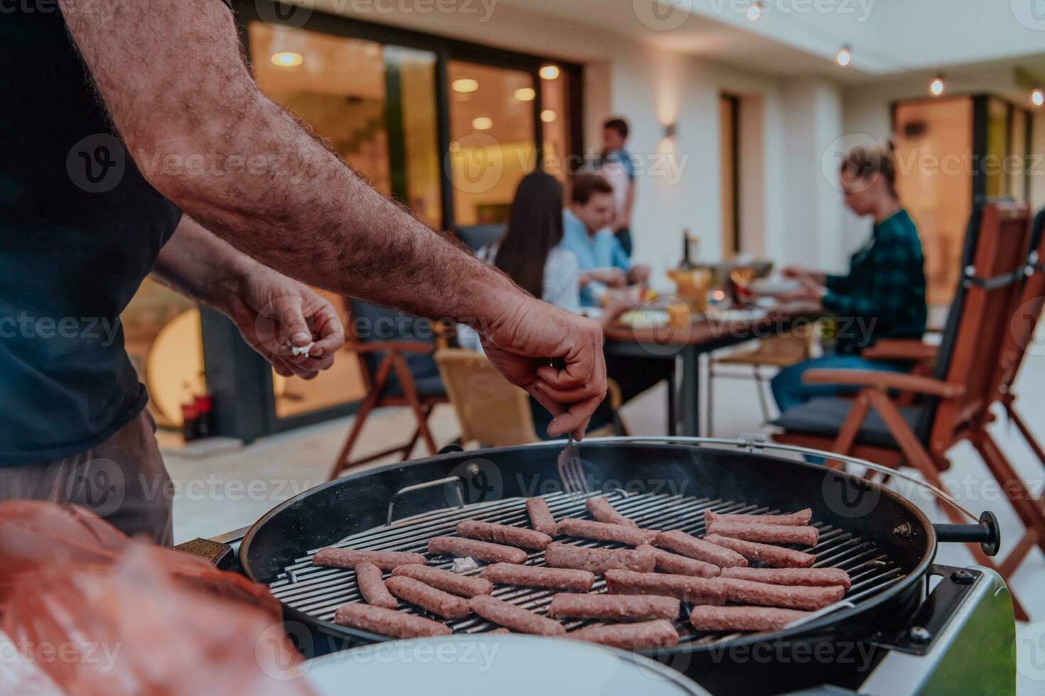 un' gruppo di amici e famiglia barbecue insieme nel il sera su il terrazza nel davanti di un' grande moderno Casa foto