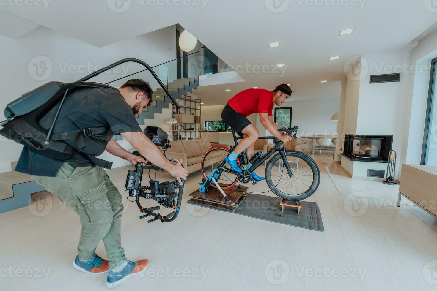 un' cineoperatore le riprese un atleta equitazione un' Triathlon bicicletta su un' simulazione macchina nel un' moderno vivente camera. formazione nel pandemia condizioni. foto