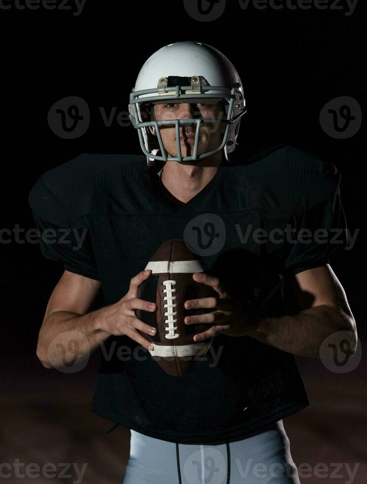 americano calcio campo solitario atleta guerriero in piedi su un' campo detiene il suo casco e pronto per giocare a. giocatore preparazione per correre, attacco e Punto touchdown. piovoso notte con drammatico nebbia, blu leggero foto