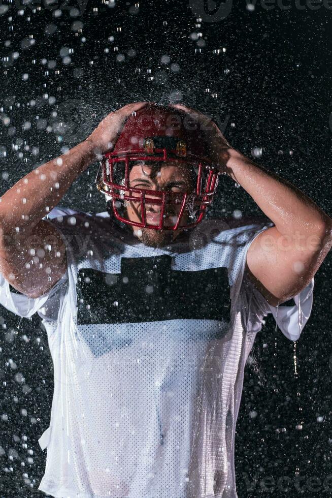 americano calcio campo solitario atleta guerriero in piedi su un' campo detiene il suo casco e pronto per giocare a. giocatore preparazione per correre, attacco e Punto touchdown. piovoso notte con drammatico nebbia, blu leggero foto