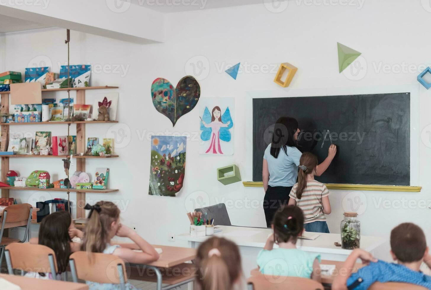 elementare scuola. il femmina insegnante porzione il bambino alunno mentre scrittura il risposta su il lavagna. foto