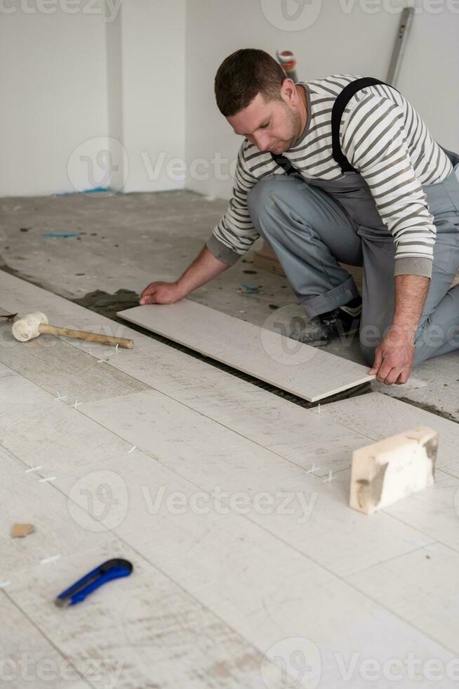 operaio che posa le piastrelle in ceramica effetto legno sul pavimento foto