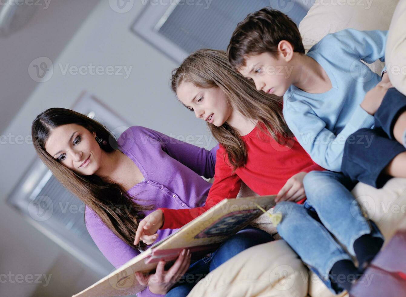 giovane mamma giocare con loro bambini a casa e lettura libro foto