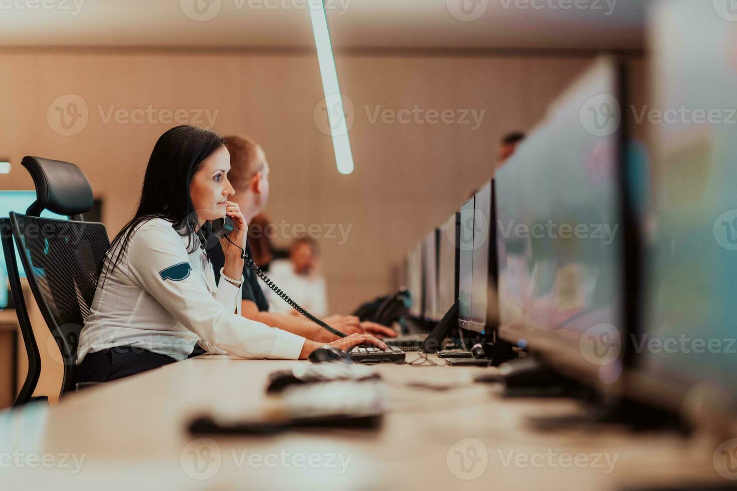 femmina sicurezza guardia operatore parlando su il Telefono mentre Lavorando a stazione di lavoro con multiplo viene visualizzato sicurezza guardie ✔ Lavorando su multiplo monitor foto