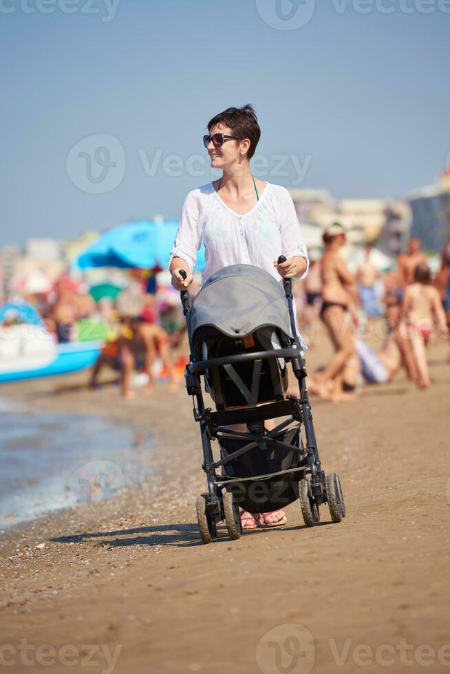 madre a piedi su spiaggia e spingere bambino carrozza foto