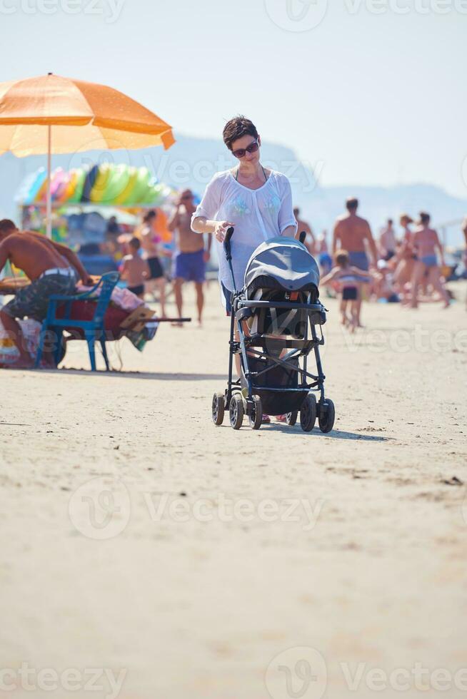 madre a piedi su spiaggia e spingere bambino carrozza foto