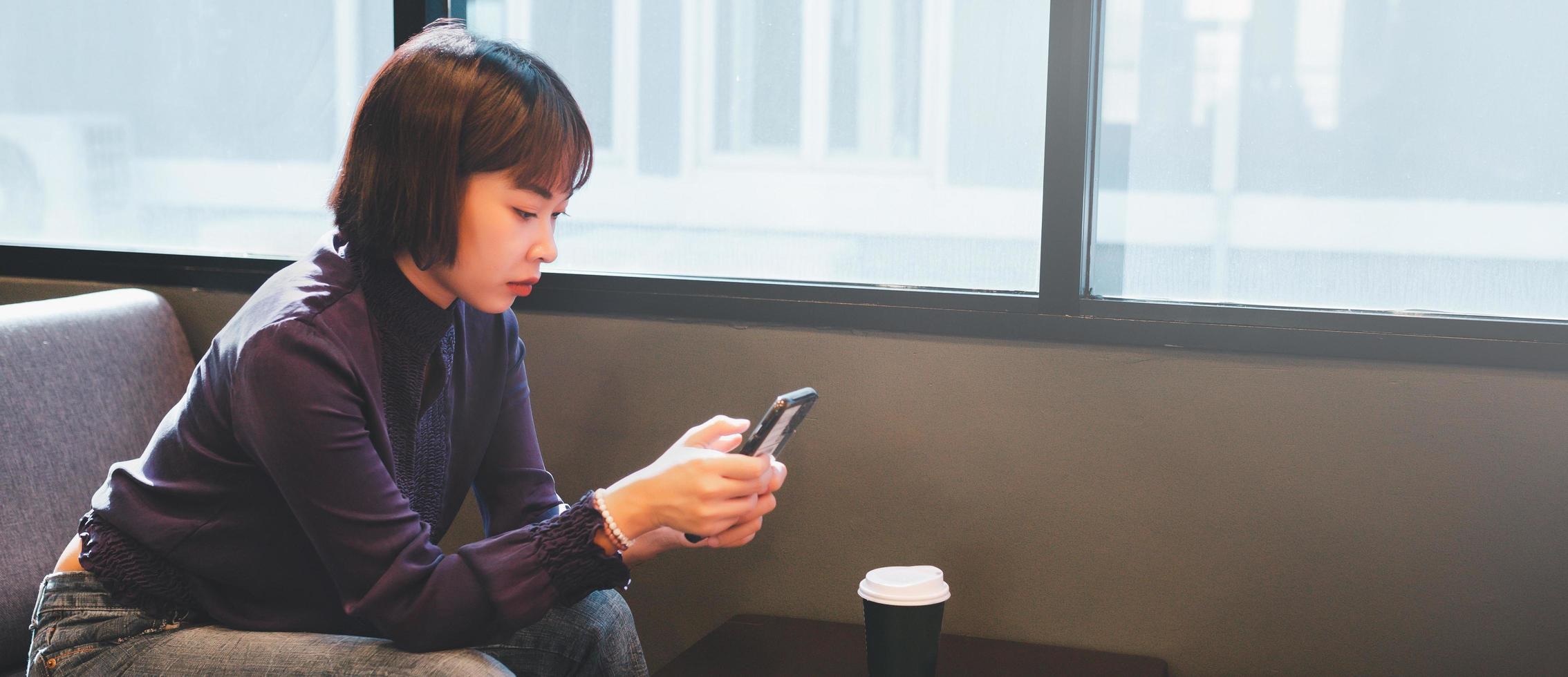 giovane donna asiatica che utilizza il telefono cellulare al cafe foto