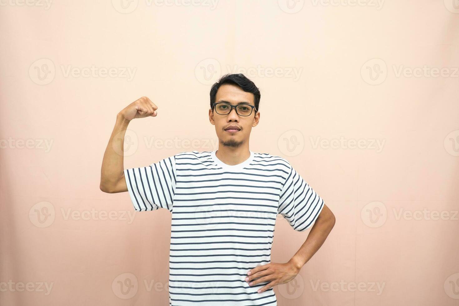 asiatico uomo con bicchieri indossare casuale a strisce camicia, cazzotto cazzotto posa, indicando forte o pronto per combattere. isolato beige sfondo. foto