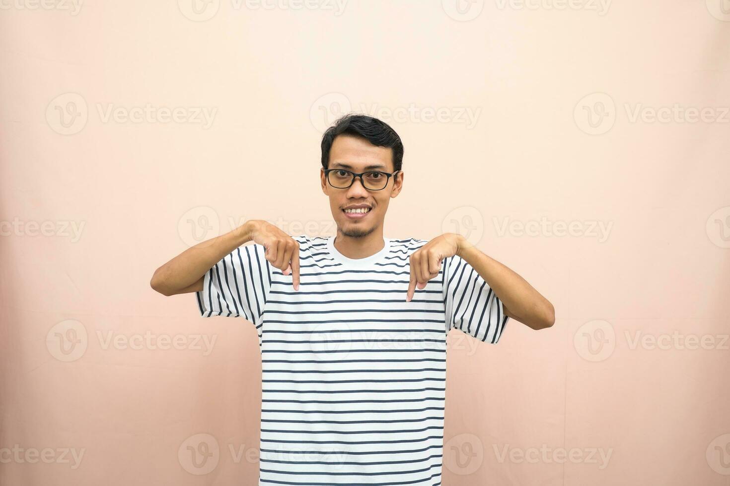 asiatico uomo con bicchieri indossare casuale a strisce camicia, sussurrando posa mentre puntamento fuori uso. isolato beige sfondo. foto