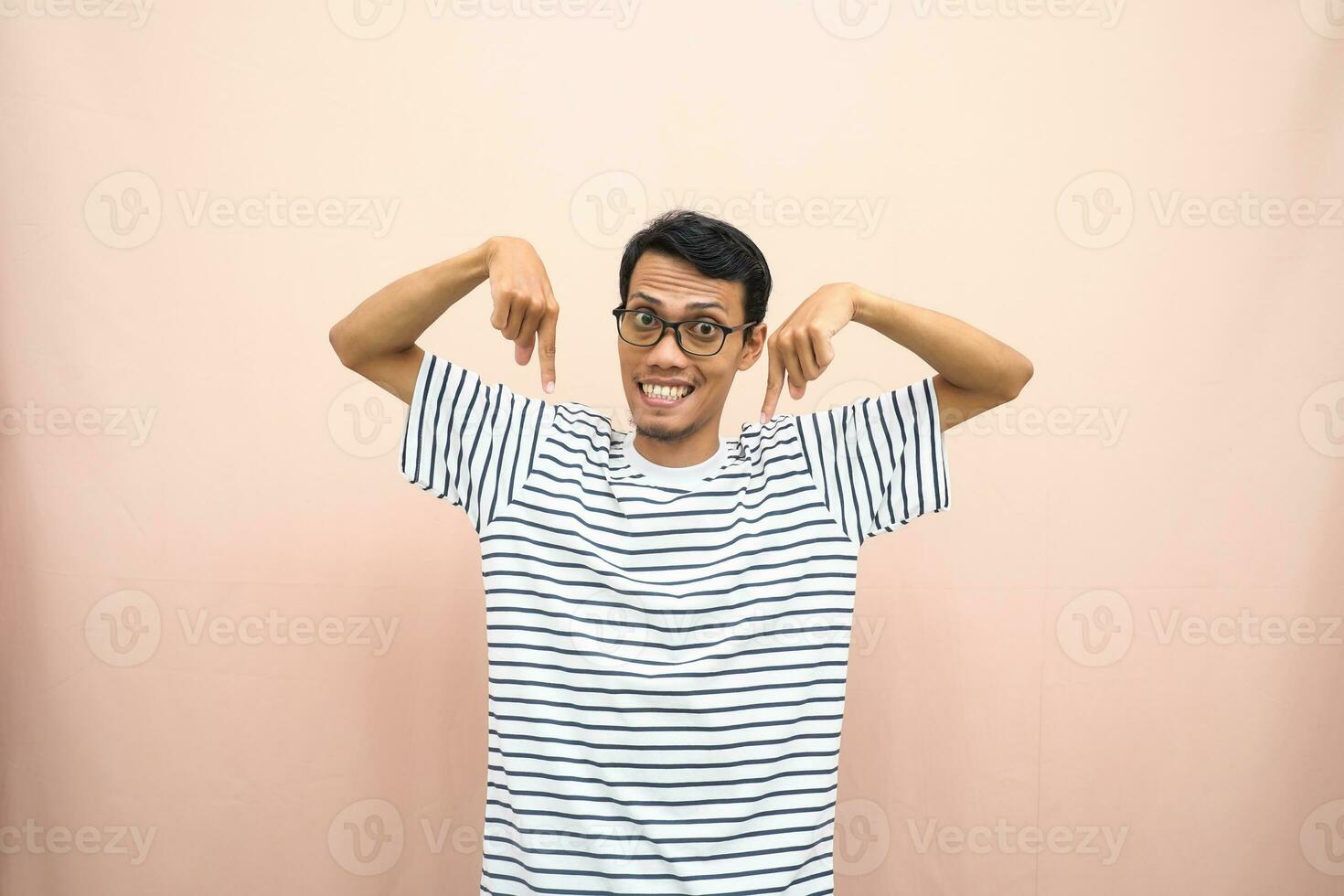 asiatico uomo con bicchieri indossare casuale a strisce camicia, sussurrando posa mentre puntamento fuori uso. isolato beige sfondo. foto