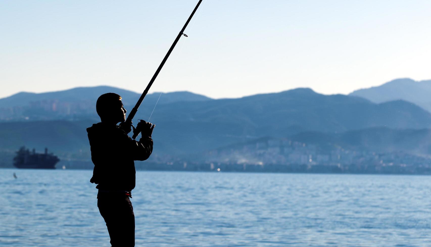 un ragazzo ombra vicino al mare che pesca foto