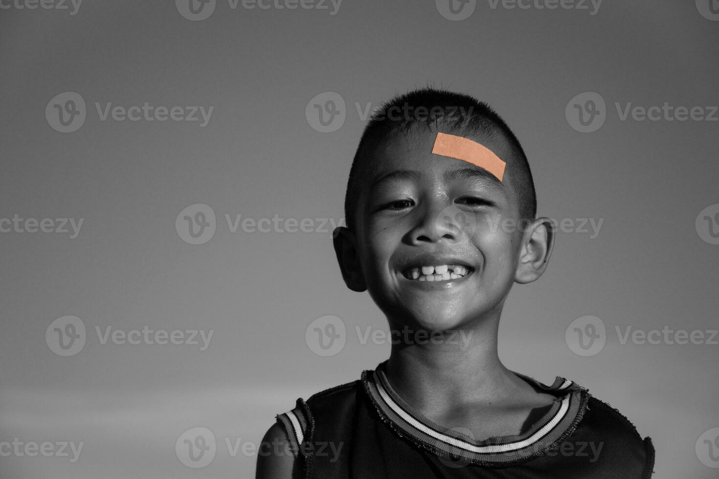 contento ragazzo Sorridi e affascinante avere plastica bendare su testa ferita, bambini incidenti e primo aiuto, bambini con cerotto, fisico ferita, stile di vita, felice incidente, nero e bianca immagine,cielo sfondo. foto