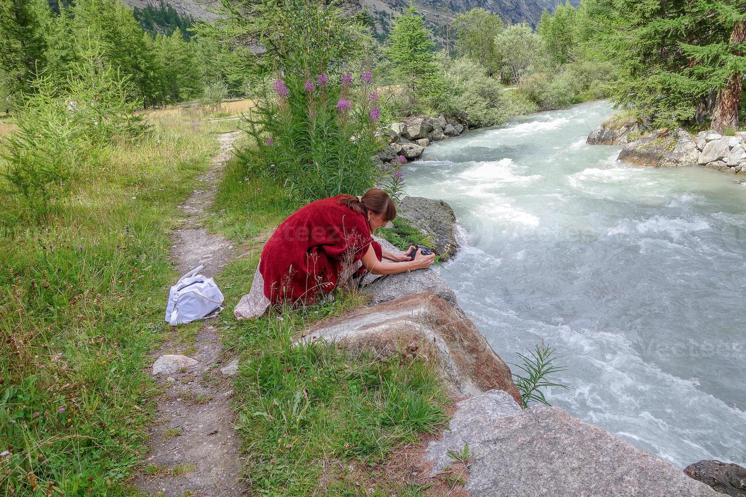 donna piegata sopra il fiume di montagna a fotografare il paesaggio foto