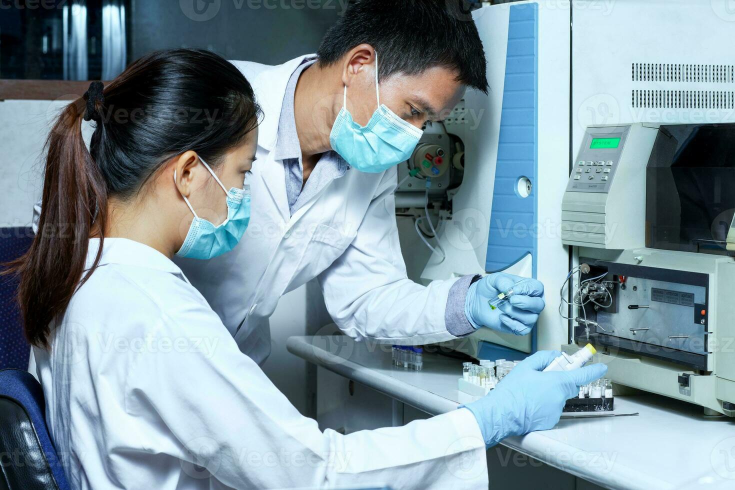 il maschio ricercatore verificato il campione nel il fiala per analizzare di liquido cromatografia massa spettrometria lc-ms strumento nel il laboratorio e informato un' femmina scienziato prima analisi. foto