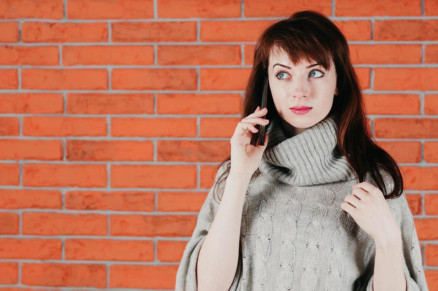 una bella ragazza che parla al cellulare, occhi sorpresi, in maglione grigio foto