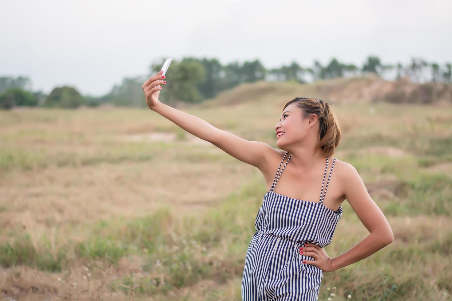 giovane donna in piedi usando il suo smartphone selfie nel campo in erba. foto