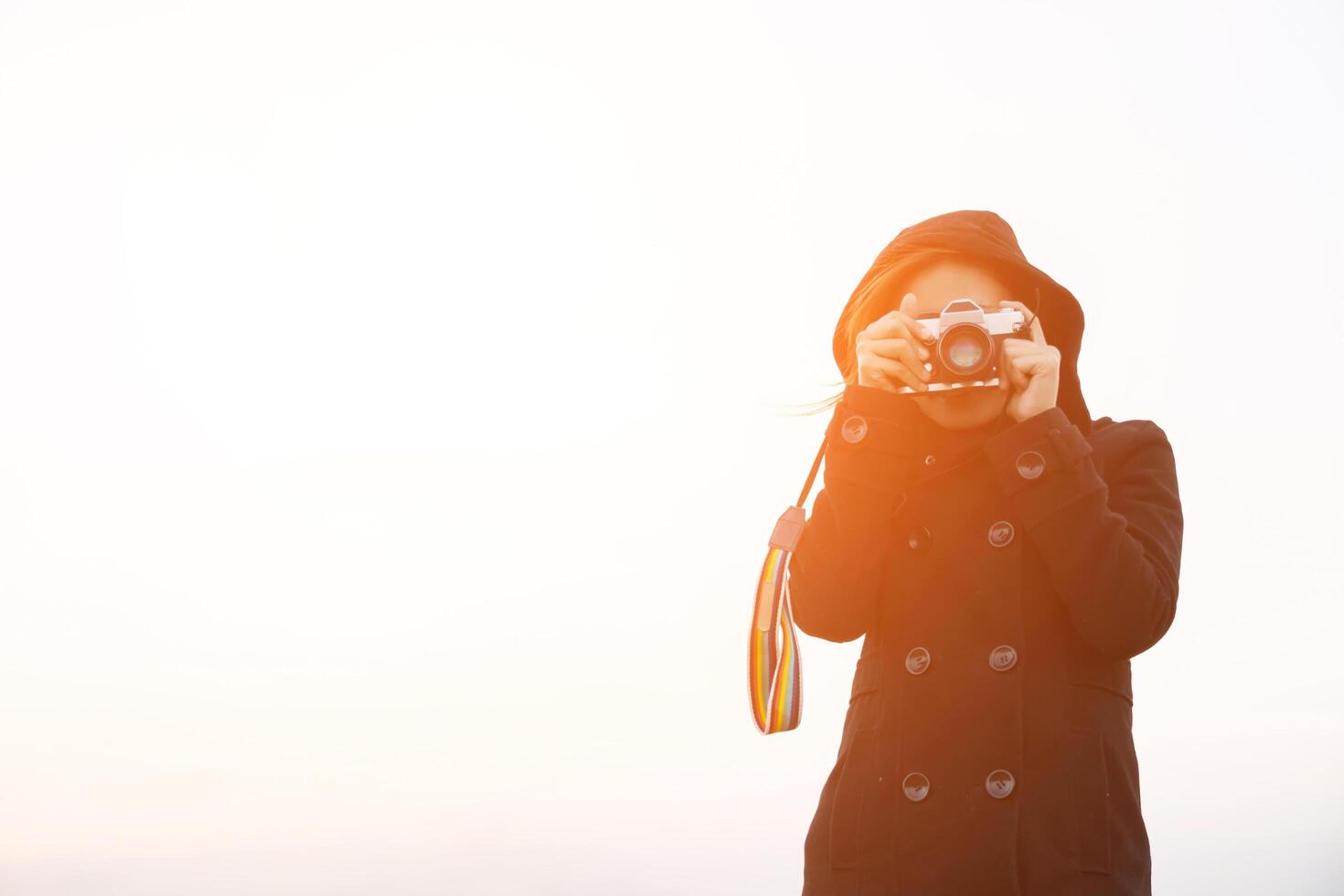 giovane donna che indossa un cappotto nero in piedi porta una fotocamera retrò foto