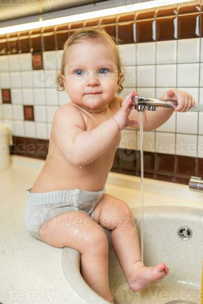 ritratto di un' contento bambino chi giochi e spruzzi nel il cucina Lavello foto