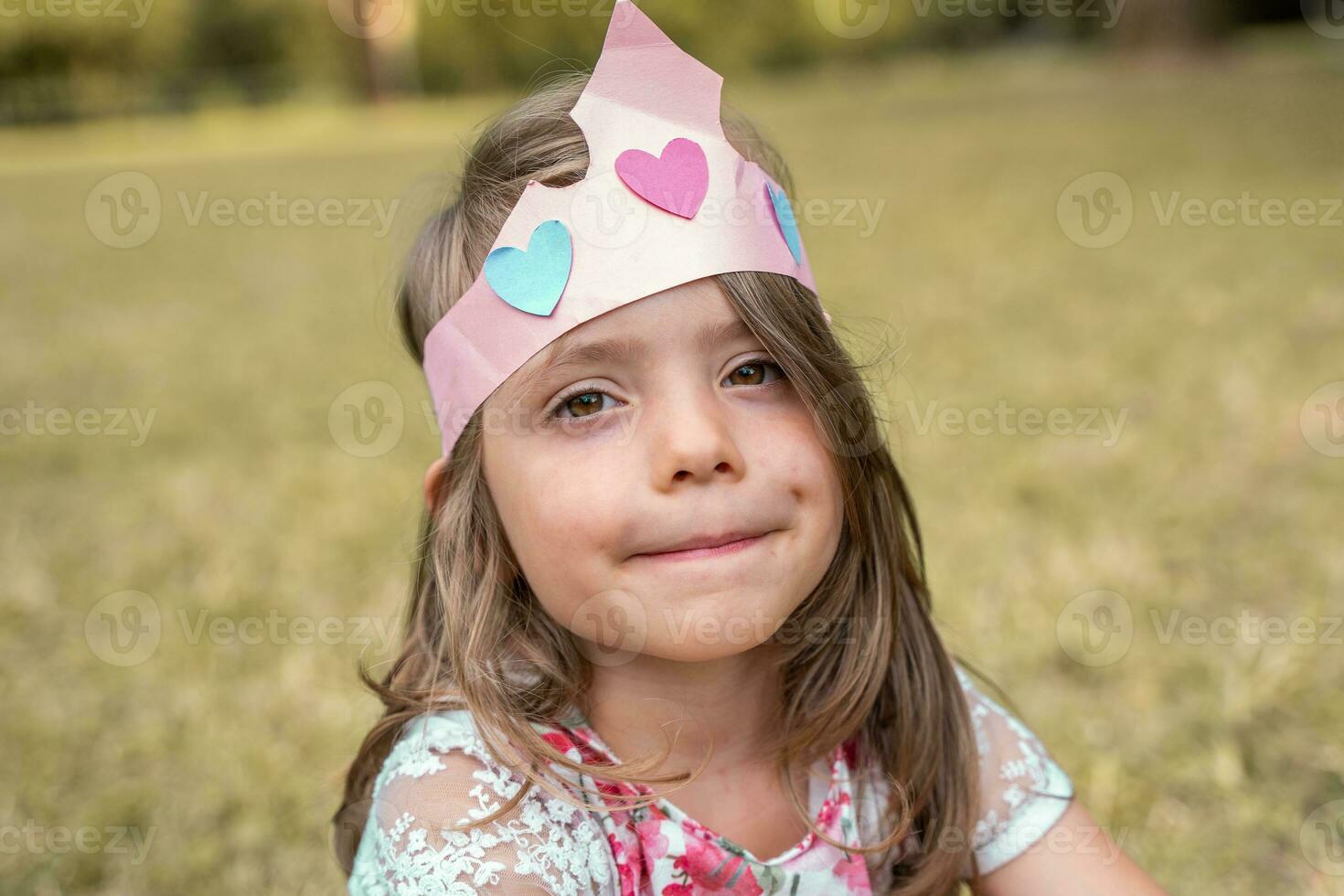 ritratto di carino ragazza con un' carta corona seduta nel un' pubblico parco foto