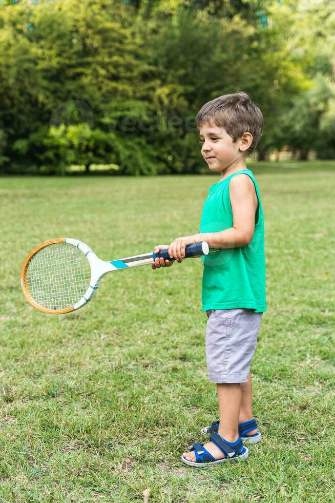 sorridente carino bambino giocando con un vecchio tennis racchetta nel un' pubblico parco foto