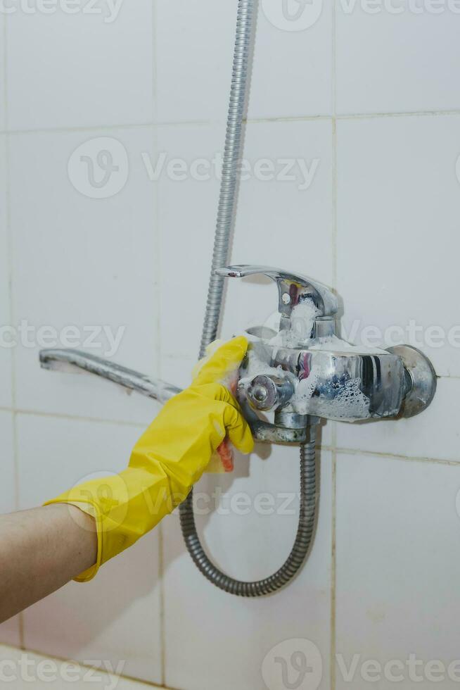 casalinga pulizia bagno rubinetto e doccia rubinetto. domestica nel giallo protettivo guanti lavaggio sporco bagno rubinetto. mani di donna lavaggio bagno foto