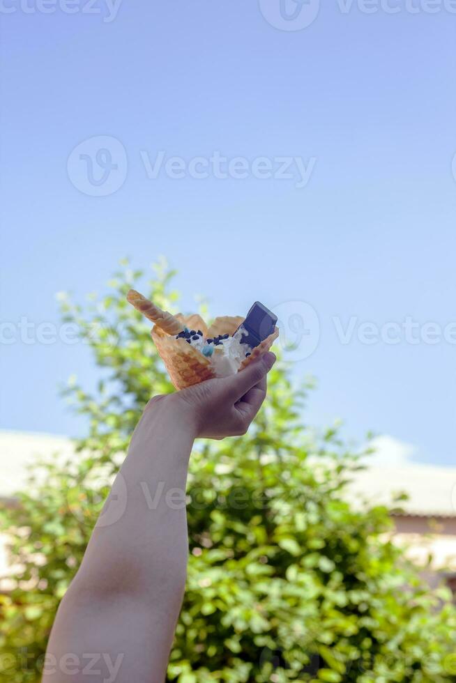 giovane donna Tenere delizioso ghiaccio crema con cialda durante un' picnic a natura. estate cibo concetto. giovane adulto mangiare delizioso ghiaccio crema con un' bastone su un' luminosa estate giorno. foto