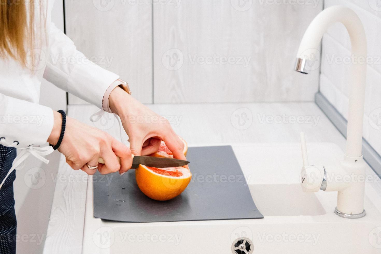 le mani della donna che tagliano il pompelmo fresco sulla cucina foto