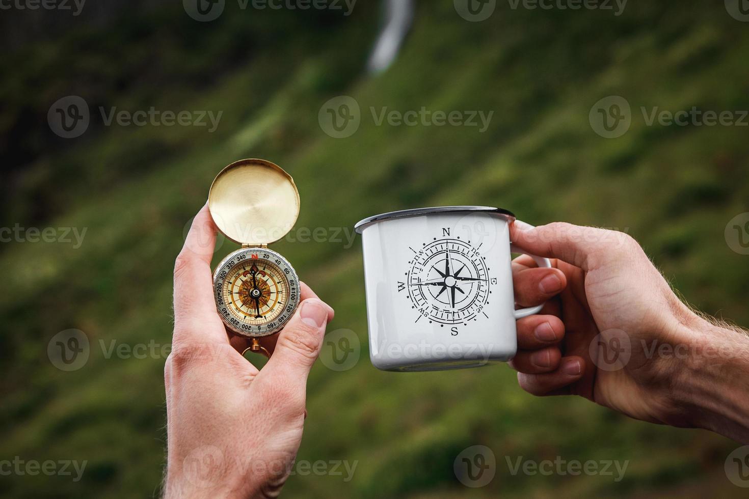 tè in una tazza di metallo turistica e una bussola in mano sfondo naturale foto