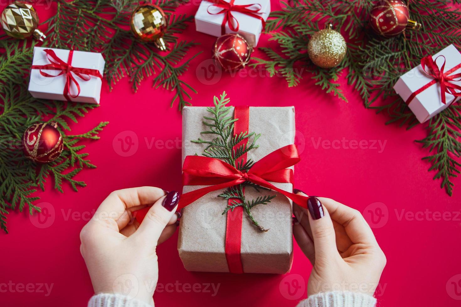 le mani tengono una bella confezione regalo con fiocco su sfondo rosso foto