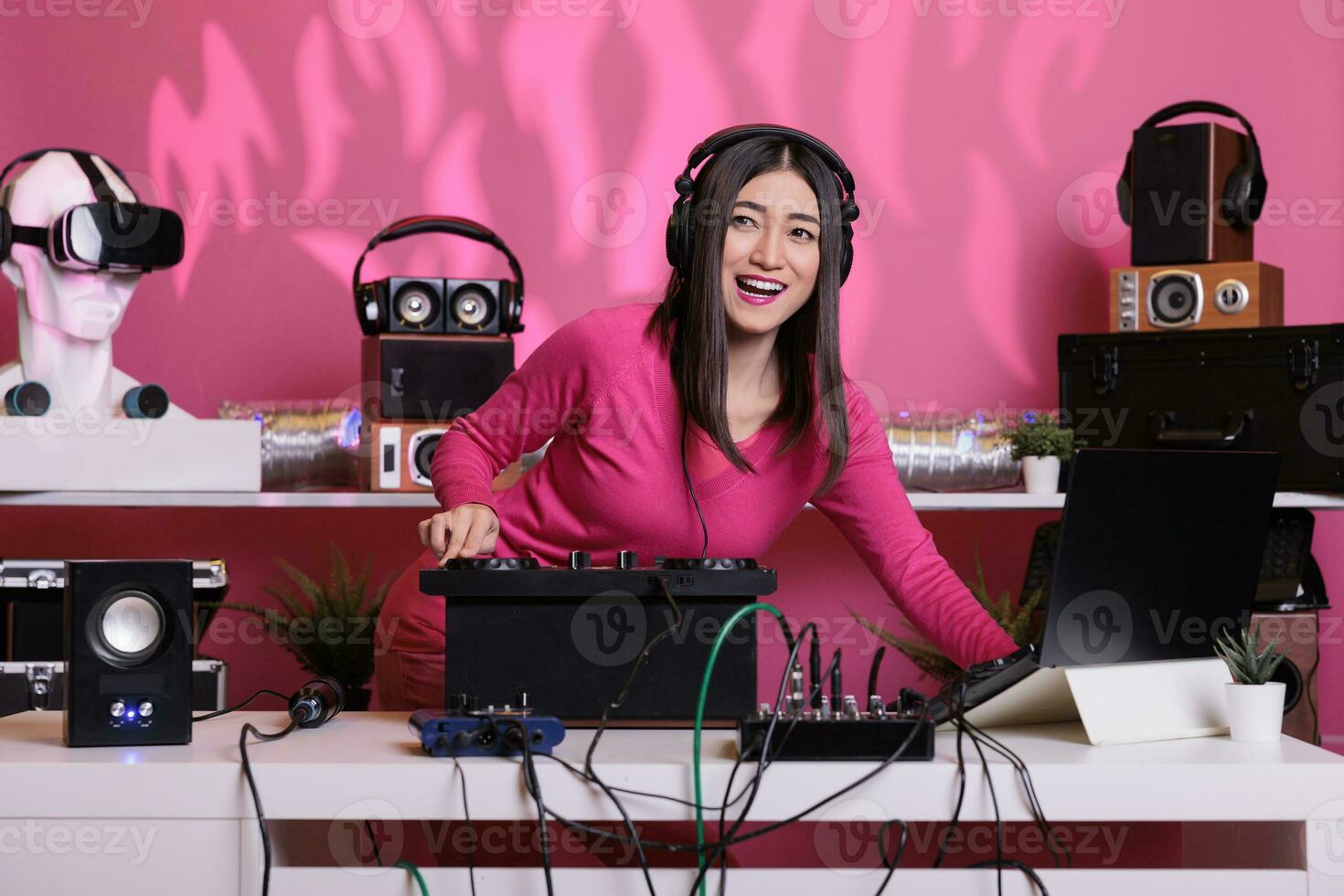 asiatico musicista giocando elettronico musica utilizzando professionale giradischi mentre in piedi a dj tavolo nel studio al di sopra di rosa sfondo. artista fare prestazione a discoteca con Audio attrezzatura foto