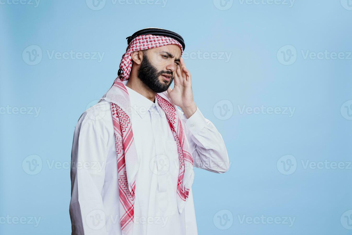 musulmano uomo indossare tradizionale Abiti sofferenza a partire dal emicrania e sfregamento tempio. arabo persona nel thobe e foulard toccante testa mentre avendo mal di testa e in posa nel studio foto