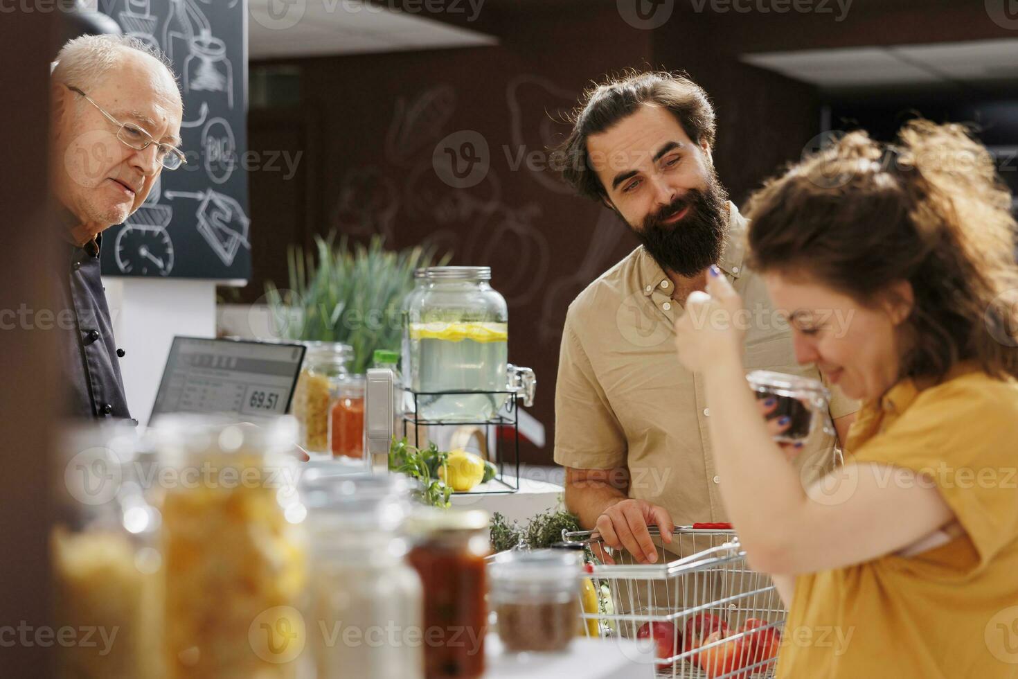 marito e moglie a zero rifiuto supermercato check-out contatore con shopping cestino pieno di biologico cibo. i clienti in attesa per loro dispensa graffette per essere ponderato con elettronico scala nel Locale negozio foto