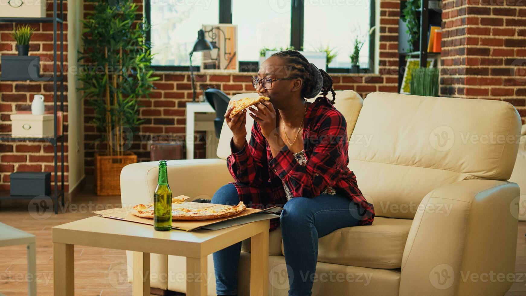 africano americano donna Guardando tv e mangiare Pizza, ridendo a commedia film nel vivente camera. giovane persona servendo veloce cibo consegna pasto e abbuffata Guardando preferito tv mostrare. foto