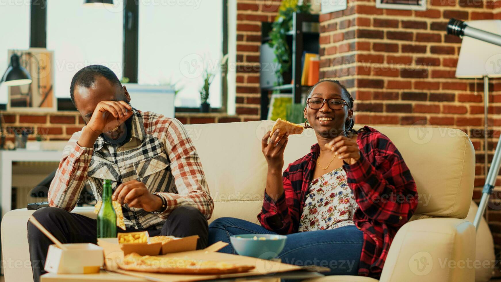 contento vita partner mangiare Pizza e Guardando film su televisione, ridendo e seduta insieme. persone nel relazione godendo portare fuori cibo per orologio preferito film su tv. tripode sparo. foto