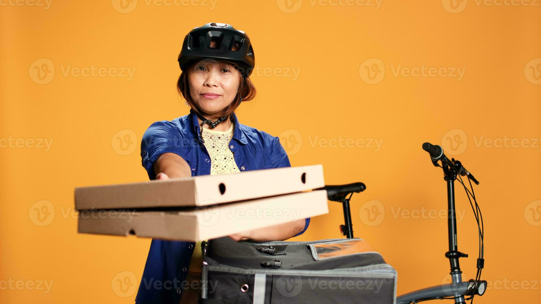 Corriere donna isolato al di sopra di arancia studio sfondo portando Pizza per cliente. bipoc bicicletta ciclista consegna ordine per cliente, assunzione veloce cibo scatole su di termico zaino foto