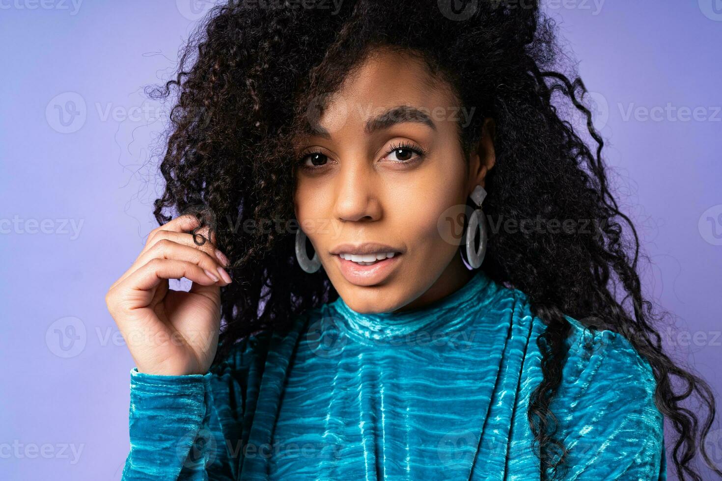 africano bellissimo donna ritratto. brunetta Riccio dai capelli modello con buio pelle nel velluto vestito in posa su blu viola sfondo. foto