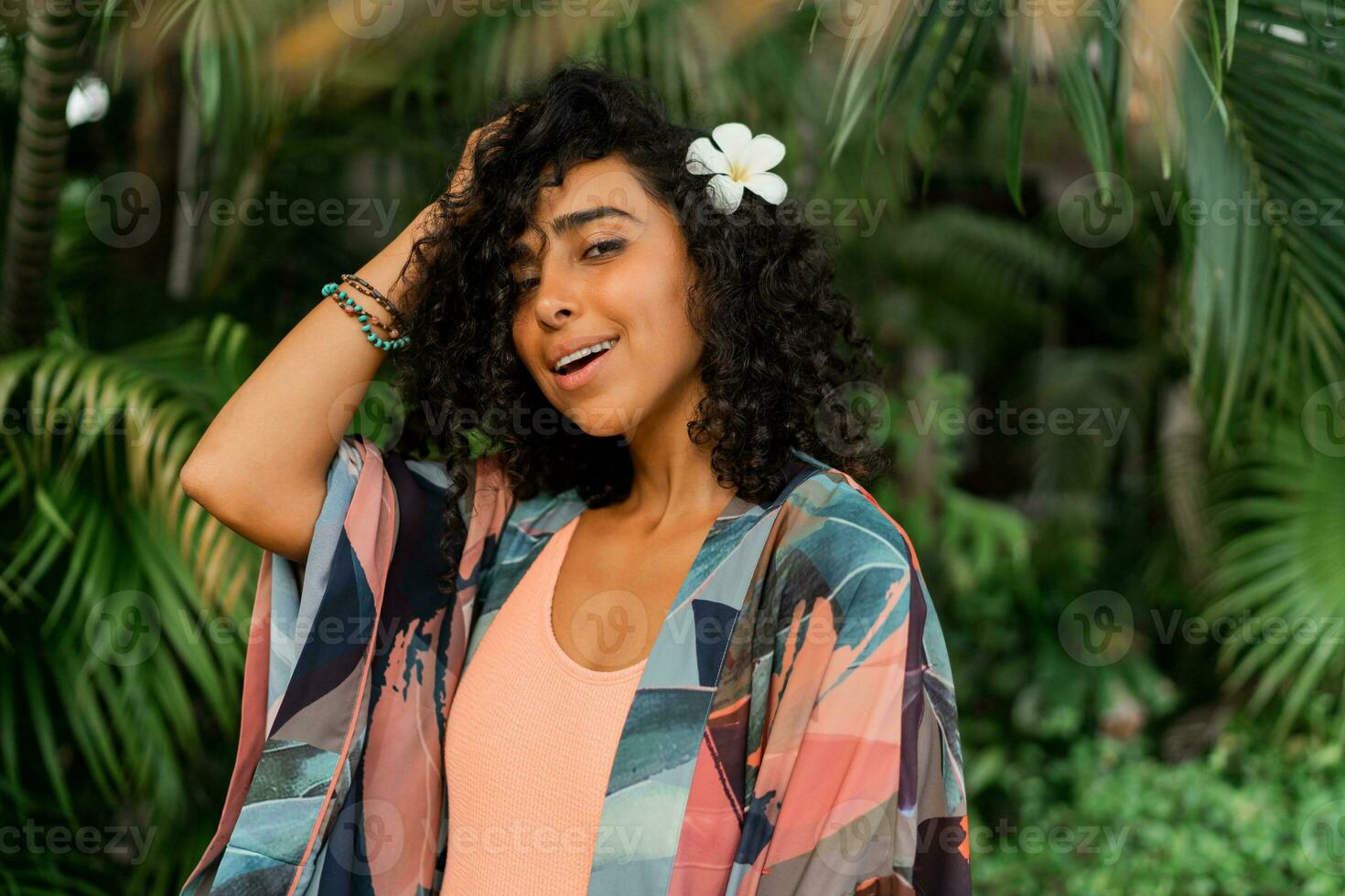 vicino su ritratto di grazioso donna con plumeria fiore nel capelli. indossare boho tropicale vestito. palma alberi su sfondo. foto