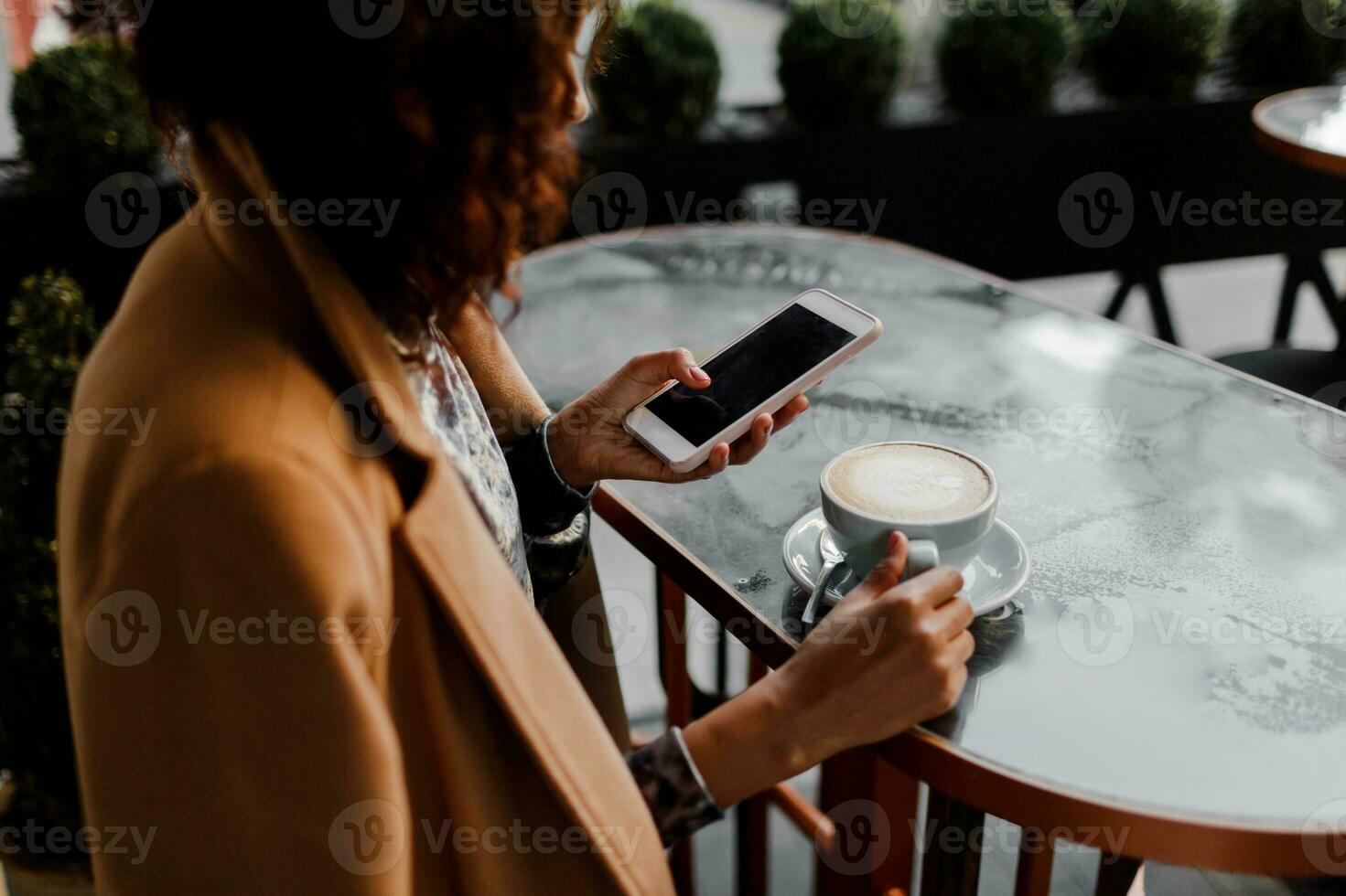 di carnagione scura donna con afro acconciatura controllo sua notizia alimentazione o messaggistica attraverso sociale reti, utilizzando gratuito Wi-Fi su mobile Telefono, sorridente, seduta a bar. foto