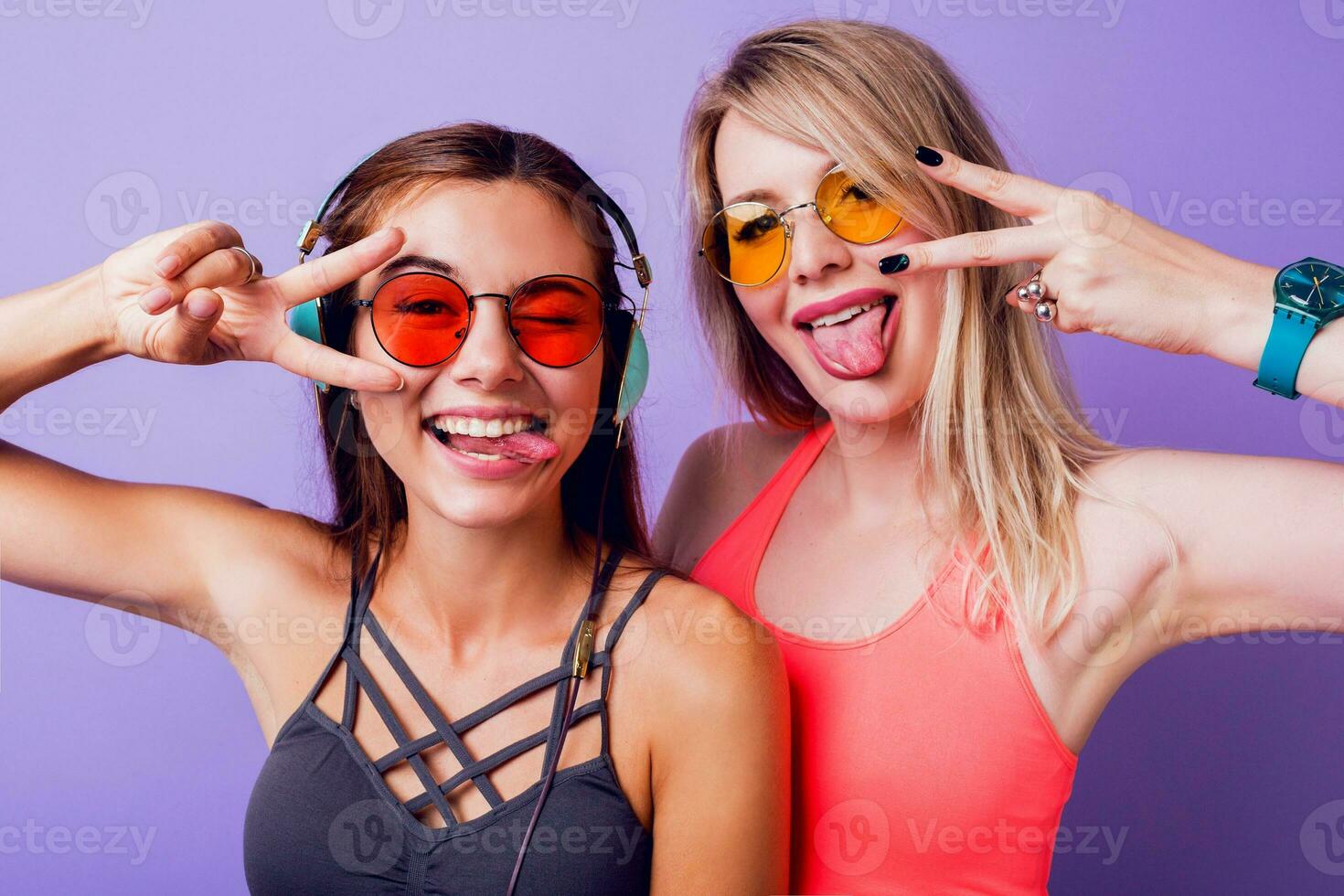 fitness ragazze Spedire aria bacio e assunzione se stesso ritratto di mobile Telefono. indossare luminosa rosa abbigliamento sportivo. elegante occhiali da sole. in posa su viola sfondo. foto