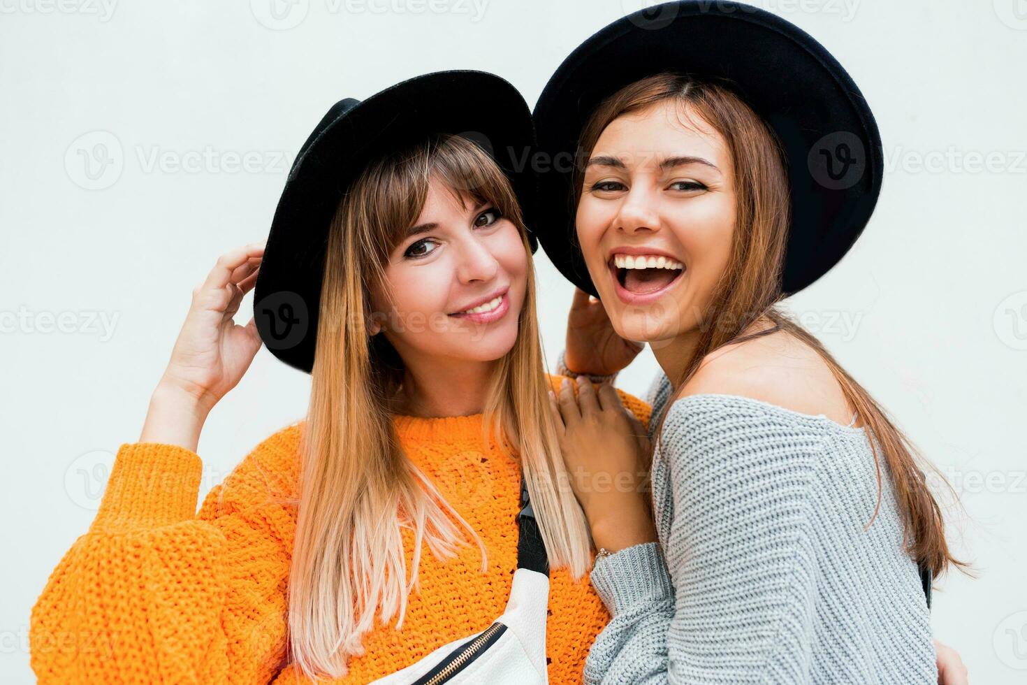 Due spensierato ragazze invio aria bacio per telecamera , in piedi al di sopra di bianca sfondo. indossare simile cappelli e a maglia maglioni. foto