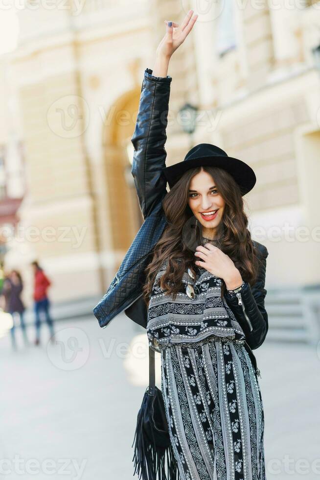 bellissimo sorprendente brunetta donna con lungo ondulato acconciatura nel primavera o autunno elegante urbano attrezzatura a piedi su il strada. rosso labbra, sottile corpo. strada moda concetto. foto