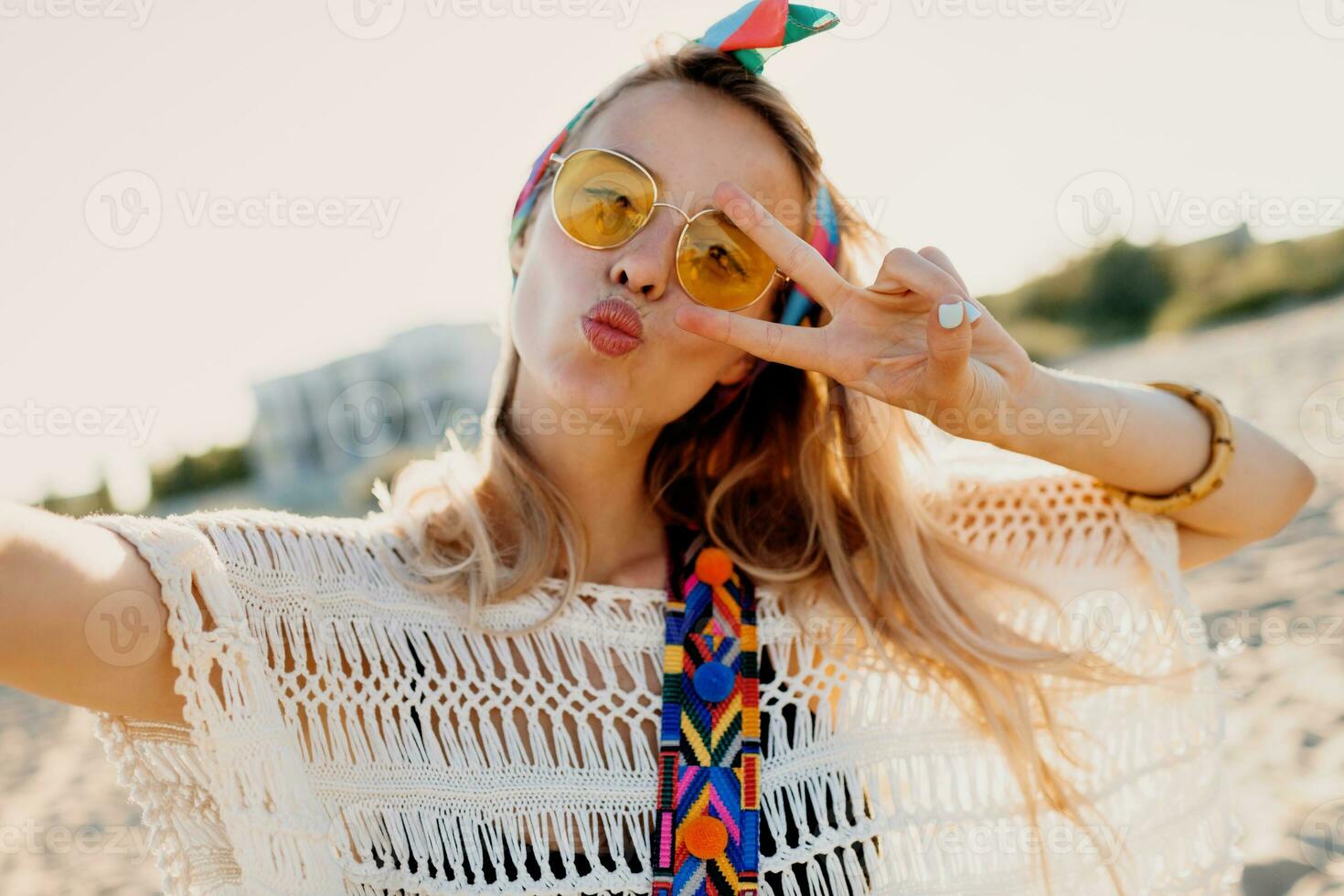 contento positivo umore. biondo giocoso ragazza con elegante fascia per capelli fabbricazione se stesso ritratto su tropicale soleggiato spiaggia. viaggio e la libertà concetto. boemo vestito. foto