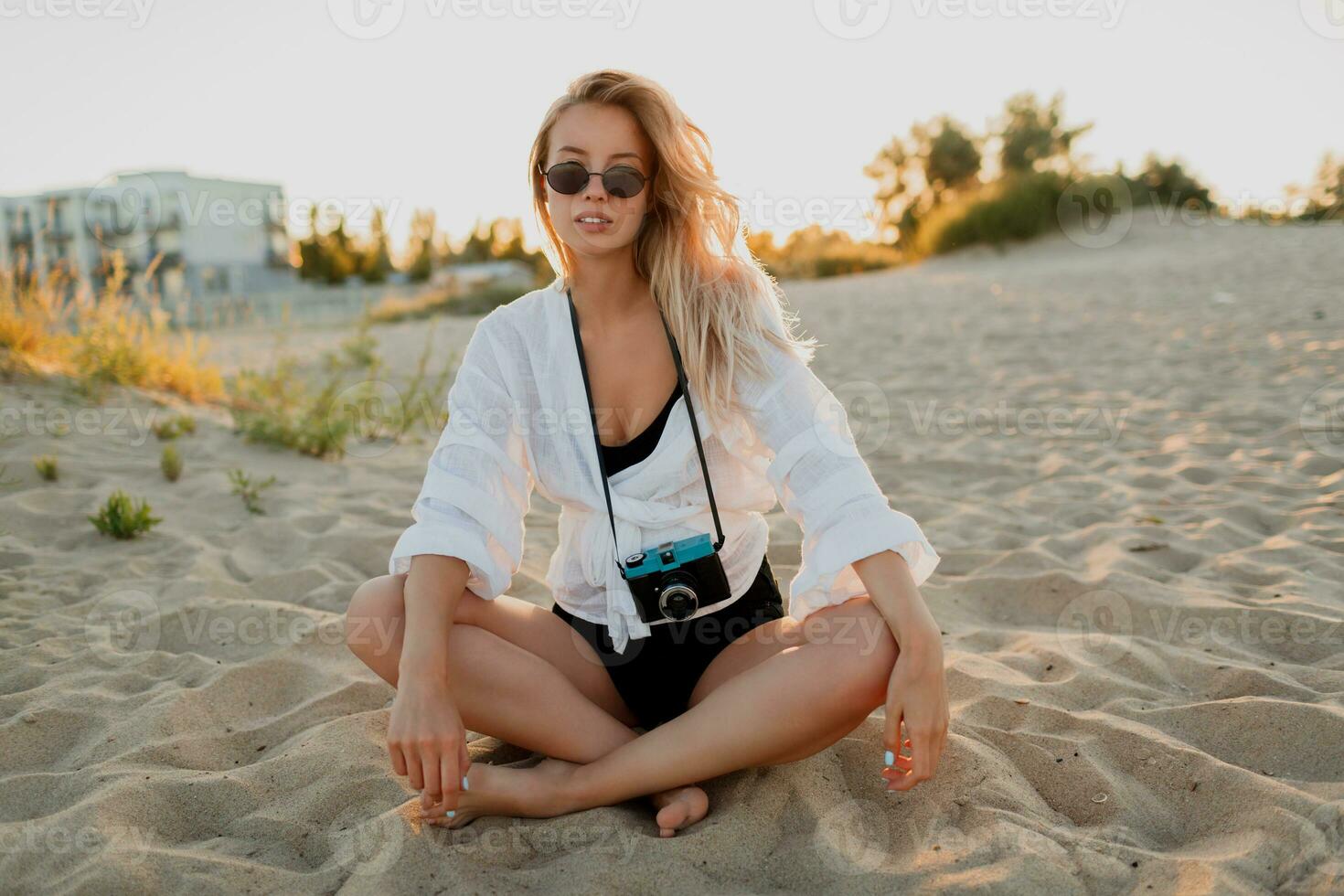 sexy donna rilassante su il spiaggia nel caldo estate sera. indossare bianca camicetta e occhiali da sole. foto